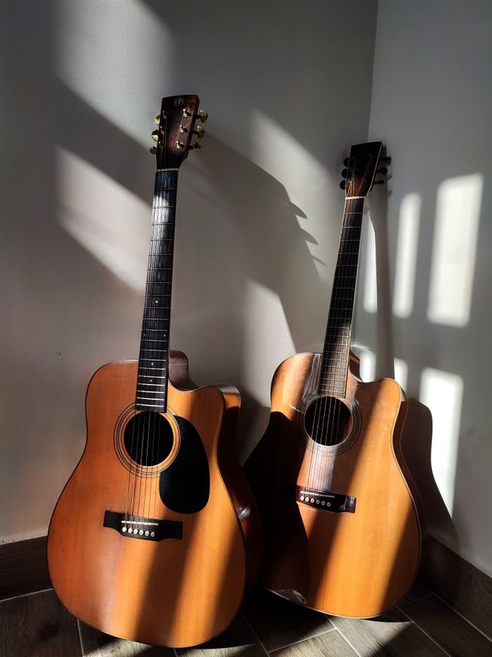 Two classic wooden acoustic guitars with shadows on a wall, creating a vintage vibe.