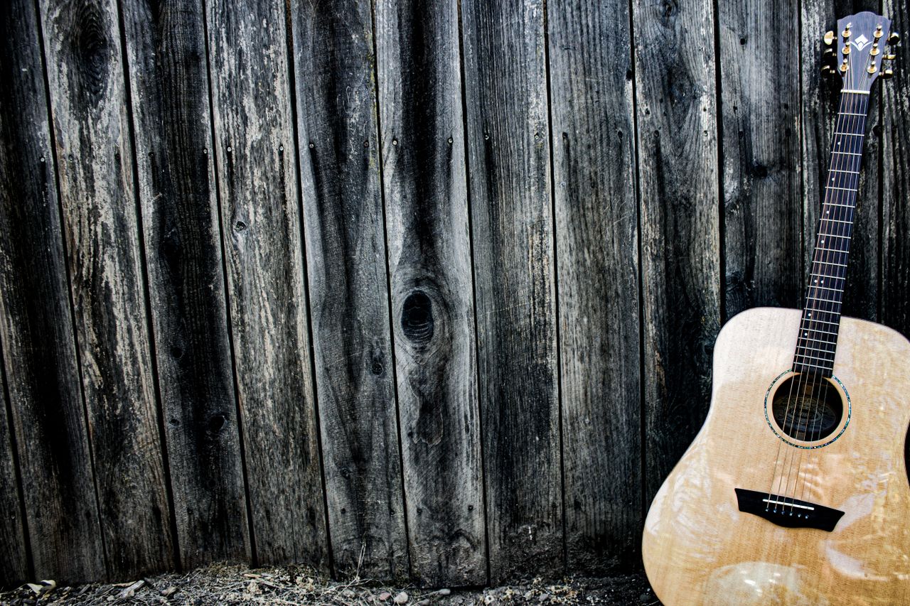 An acoustic guitar resting against a textured wooden wall, evoking a rustic musical charm.